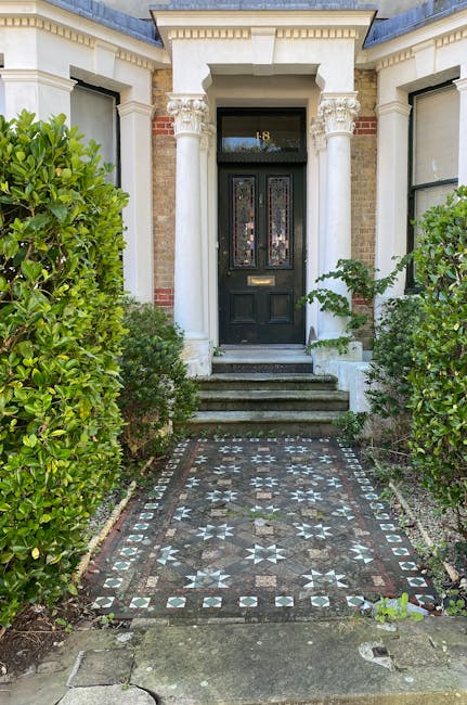 An ornate black front door with decorative stained glass panels, framed by classical white columns and detailed cornicing, leads to a Victorian-style residential entrance. The entrance is accessed via
